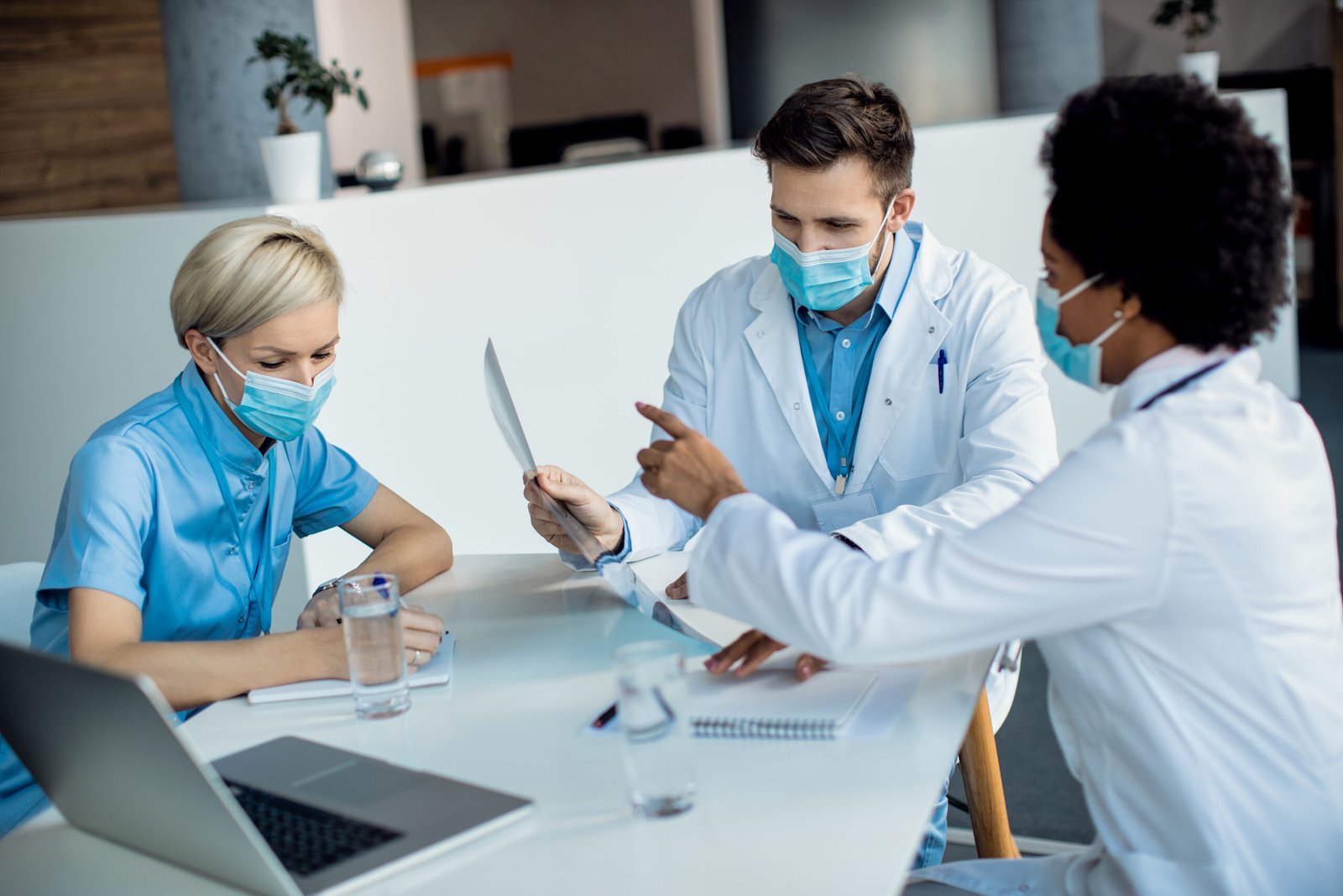 Team of medical experts examining X-ray of a patient while working at the hospital. They are wearing face masks due to COVID-19 pandemic.