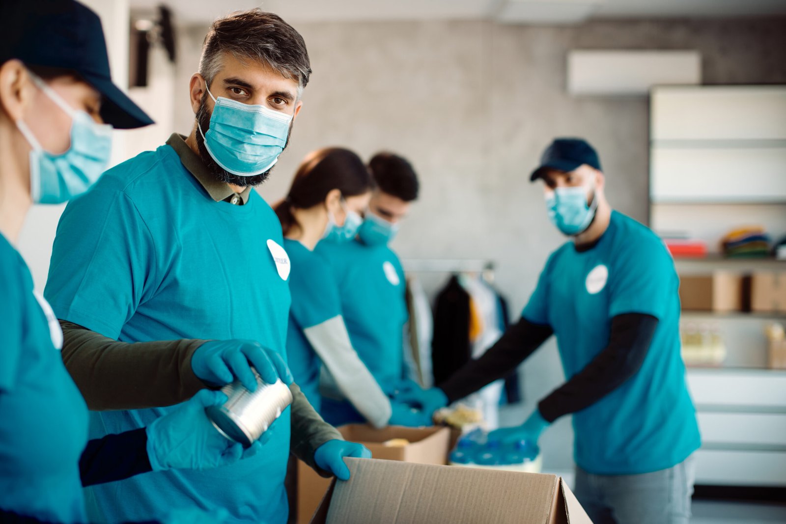 Group of volunteers packing boxes with canned food for charitable donation. Focus is on man looking at camera.