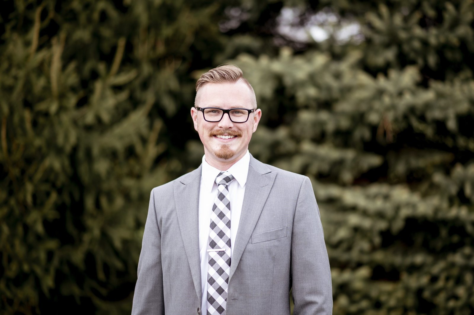 A handsome man in suit standing outdoors with blurry greenery in the background