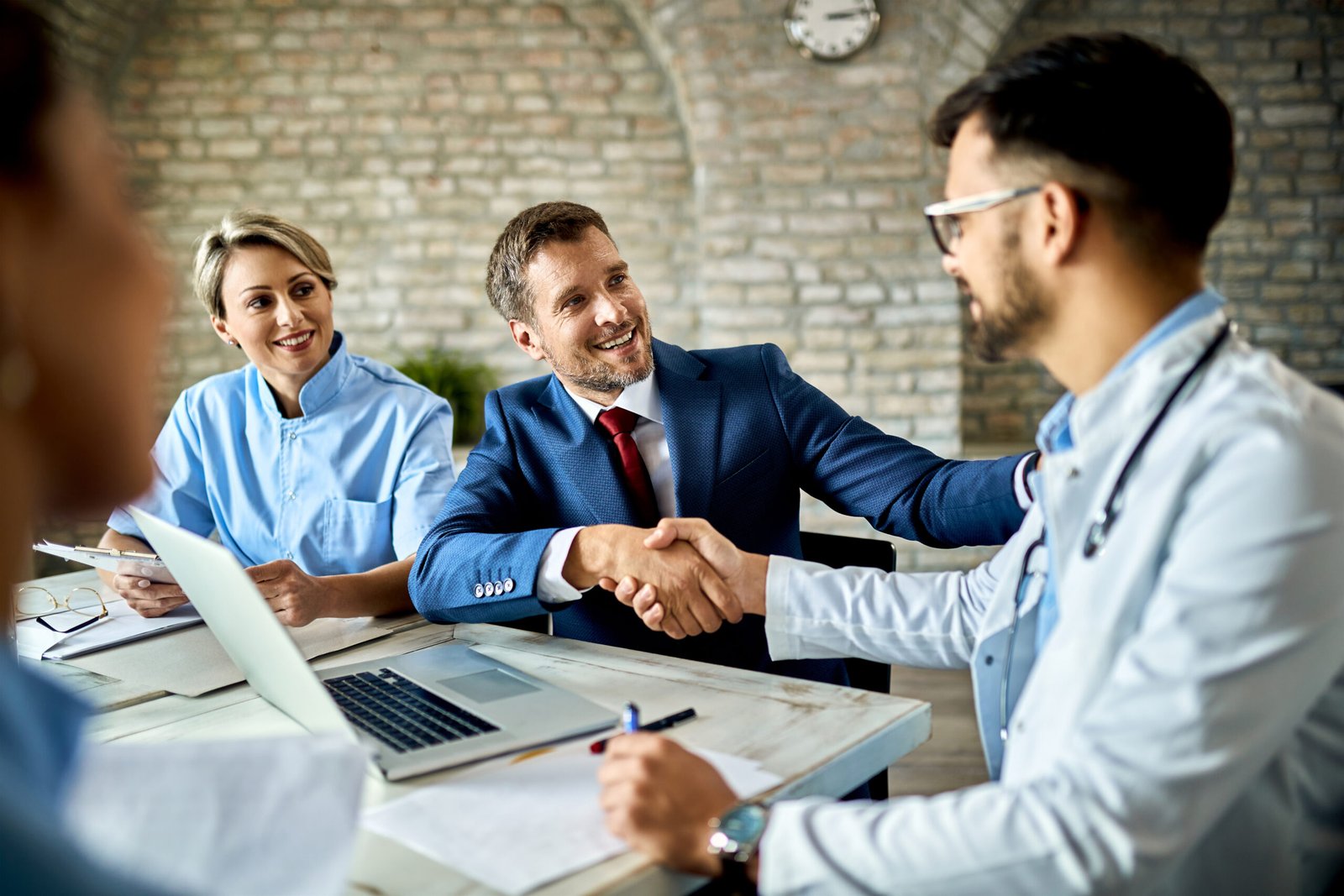 Happy financial advisor and male doctor shaking hands after successful meeting in the office.