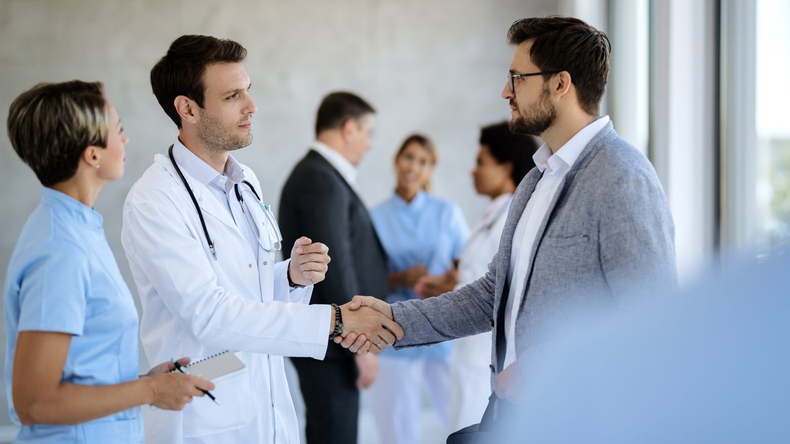 Male doctor handshaking with a businessman while meeting in a hallway at medical clinic.
